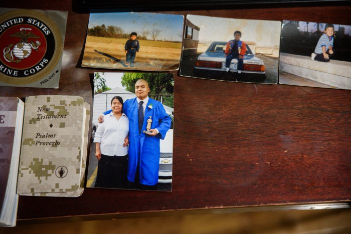 A wooden surface displays several photographs, including smaller ones of children and a large one of a graduate standing with a woman, alongside a Marine Corps emblem and camouflage patterned books.