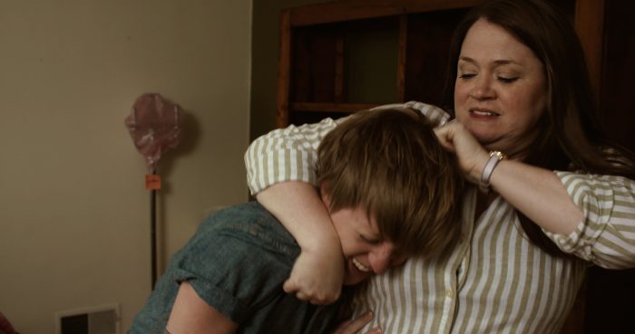 A woman in a striped shirt holds a younger person in a headlock as they grimace.